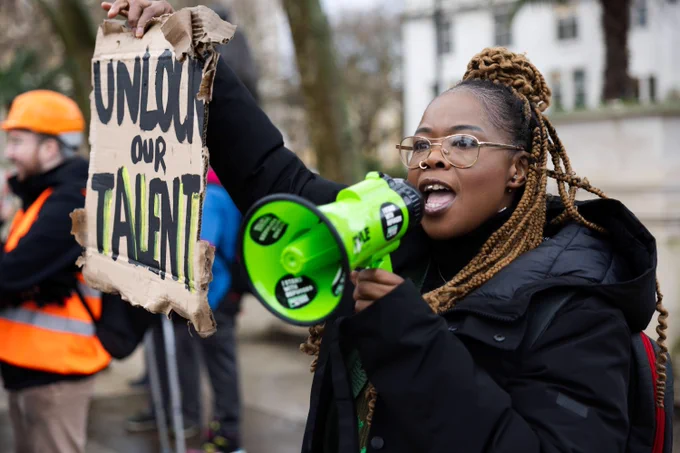 A woman holds a megaphone and a sign reading "unlock our talent"