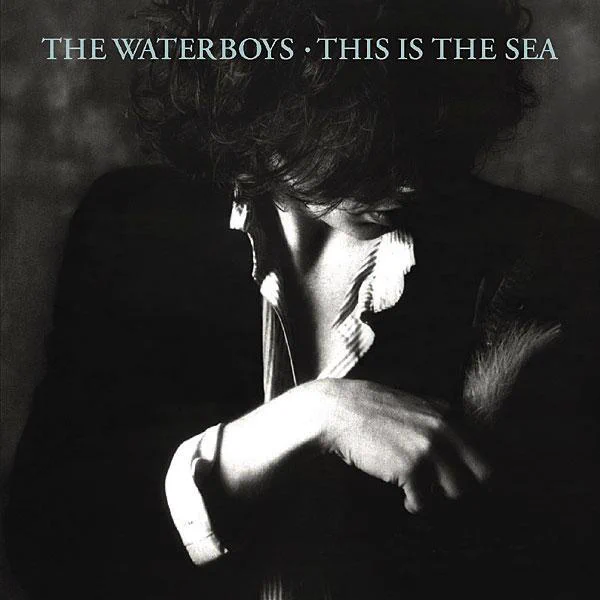 The Waterboys — This Is The Sea (1985 album cover), featuring a stark black and white portrait of Mike Scott, capturing the introspective, expansive mood that defined the era and the rise of “The Whole of the Moon.”