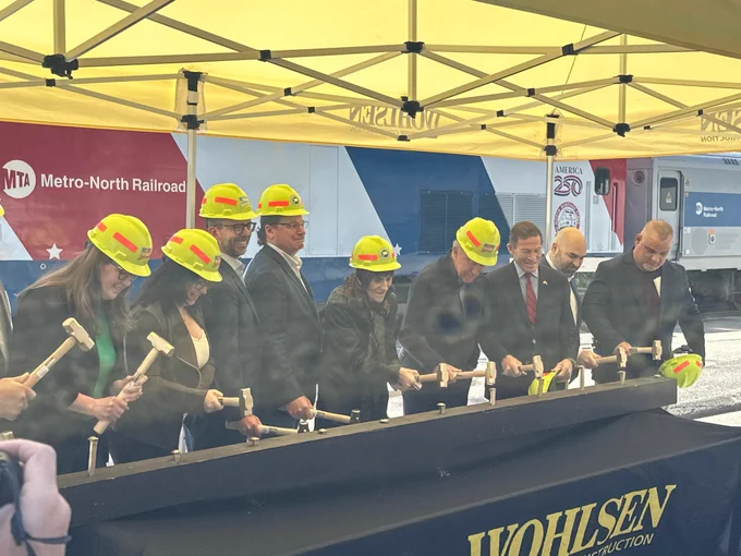 State, federal, and local officials in yellow hard hats breaking ground at a press conference to announce the start of construction to renovate four stations on the Metro-North Waterbury Branch Line. 