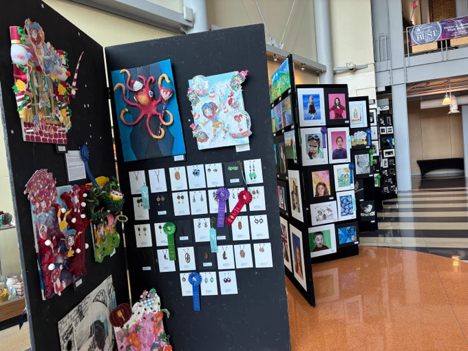 All four photos illustrate art display panels featuring colorful mixed-media sculptures, drawings, and award-winning jewelry pieces in a spacious gallery setting.
