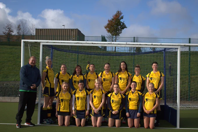 Junior girls' hockey team wearing yellow BCC IT sponsored kits posing together the BCC Director Hywel Ifans on their home pitch at Llandysul, West Wales
