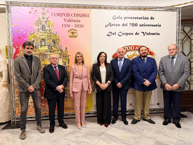 La concejala de Fiestas y Tradiciones y el concejal de Cultura y Patrimonio junto a representantes de Associació Amics del Corpus, entre otros, posan frente a un cartel del 700.º aniversario del Corpus Christi de València tras la presentación del nuevo logo de la fiesta.