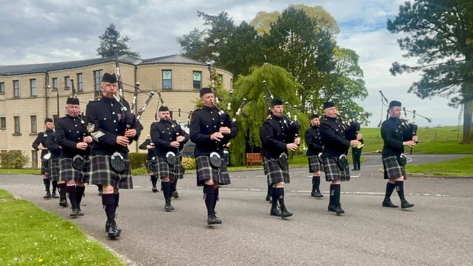 A band of bagpipers in black uniforms and tartan kilts march and play their instruments at the Passing out Parade.