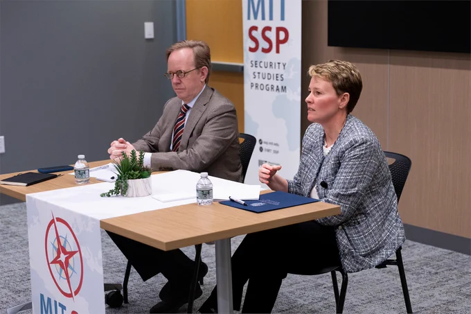 Two people are seated at a table addressing an offscreen audience.