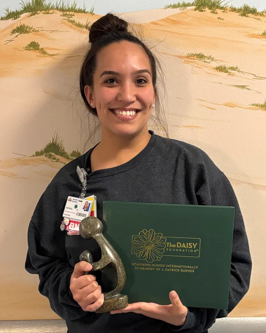 Smiling woman holding a green certificate folder and a bronze award statue against a painted desert background.