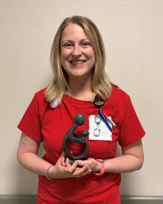 Person in red shirt holding a black abstract sculpture of a parent and child embracing.