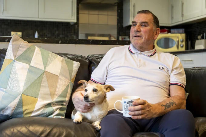 An older man sits on a sofa with his dog