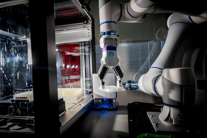 Robotic arm with precision gripper handling a small white object inside a high-tech lab environment.