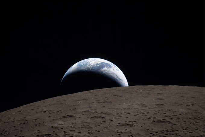 Earth rises above the Moon\u2019s cratered horizon, appearing as a blue-and-white crescent against the blackness of space. The lunar surface in the foreground is gray and pitted with craters, stretching across the lower half of the image. Credit: NASA