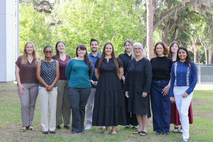11 people smiling and standing outside in a line.