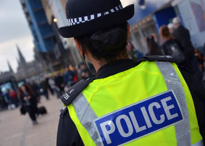 A police officer in a high-visibility yellow vest with "POLICE" written on the back, standing in a busy street.