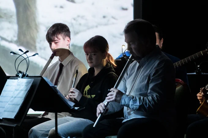 Young musicians are illuminated by colourful images on the big screen.