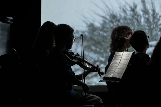Young musicians are illuminated by colourful images on the big screen.