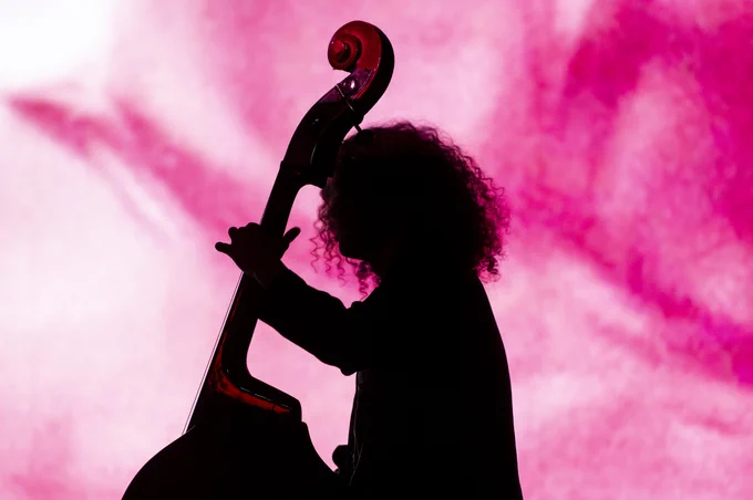 A young musician playing a large string instrument, illuminated by colourful images on the big screen.
