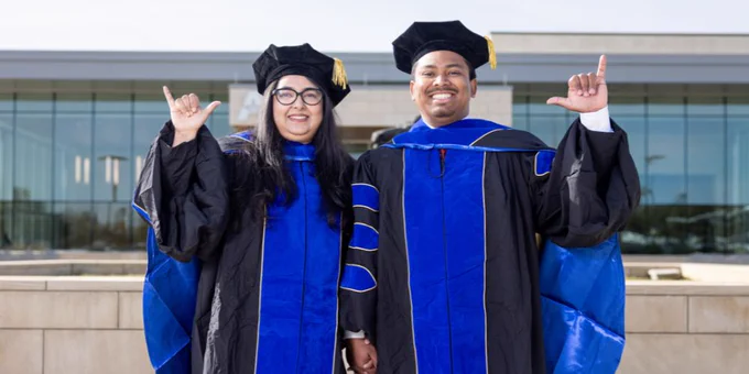Photo of married doctoral graduates Rashna Sharmin, left, and Akash Talukder in graduation regalia outside the University Center.