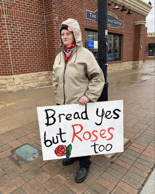 A comrade holding a sign saying “Bread yes but roses too”