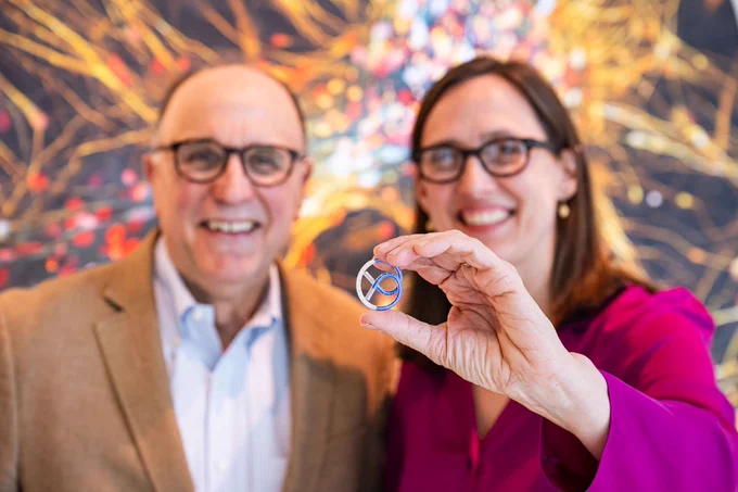 Michael Cima and Karen Daniels smiling - Karen is holding a pretzel-shaped device. 