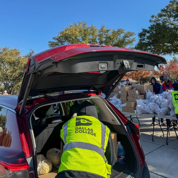 Dallas College volunteer helping to load food into the back of a car.