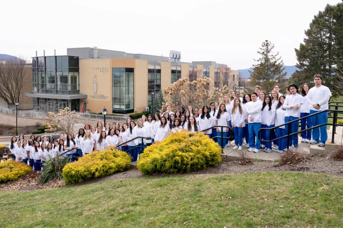 A large group of graduating nursing students in Mount branded scrubs posing for a picture in front of Aquinas Hall.
