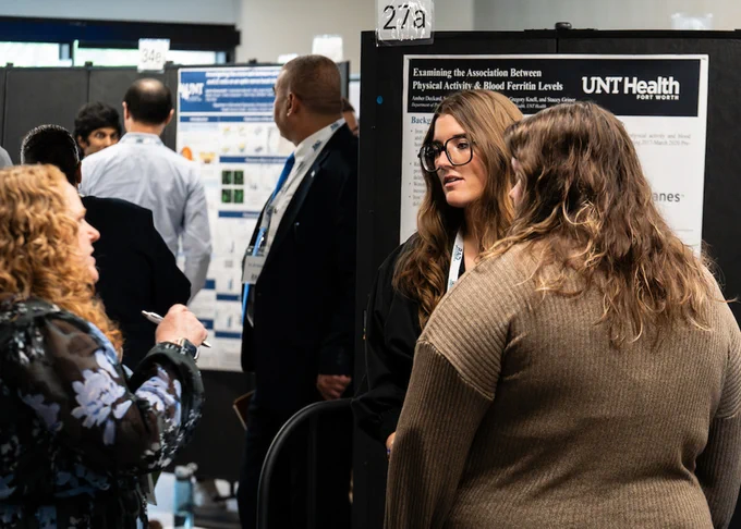 A group of individuals engaged in conversation near a UNT Health Science Center poster presentation at a conference or academic event.