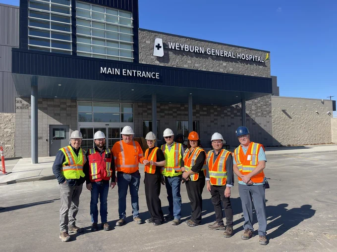 Group of people in orange and yellow safety vests in front of the new Weyburn Hospital 
