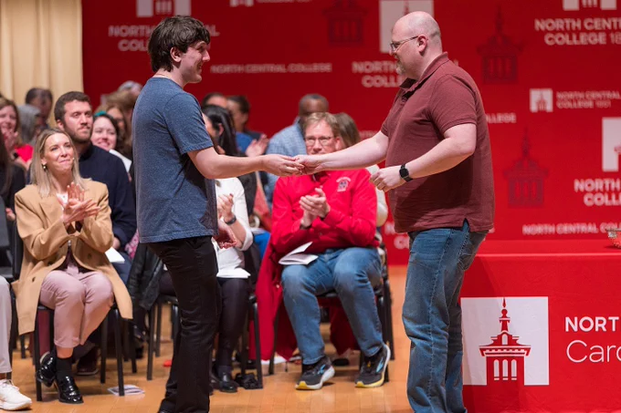 A photo of a staff member giving a Cardinal First pin to a soon-to-be-graduate.