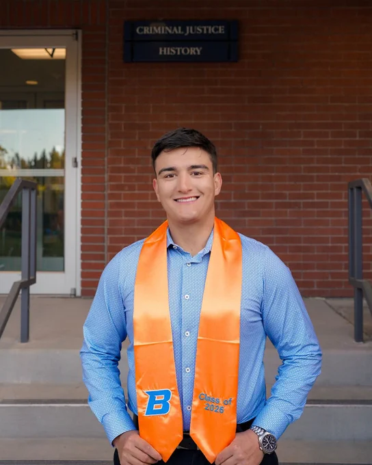 Boise State criminal justice major smiling wearing their orange stole for their graduation photos. 
