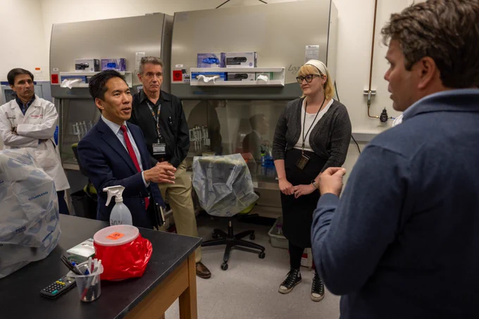 A group of people are engaged in a discussion in a laboratory setting, surrounded by scientific equipment.
