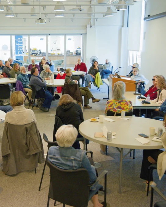 A conference room filled with round tables populated by people in chairs