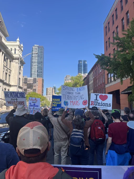 Signs saying “HEALTHCARE NOT WARFARE,” “Liberty and Justice for all means EVERYONE,” “MAKE POLLUTERS PAY,” “SAVING EARTH:
CHEAPER THAN TERRAFORMING MARS,” and “I ❤️ RUnions.”