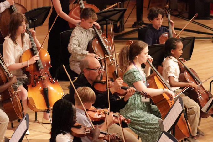 Young musicians playing cellos and violins together in a concert hall during a live orchestral performance.