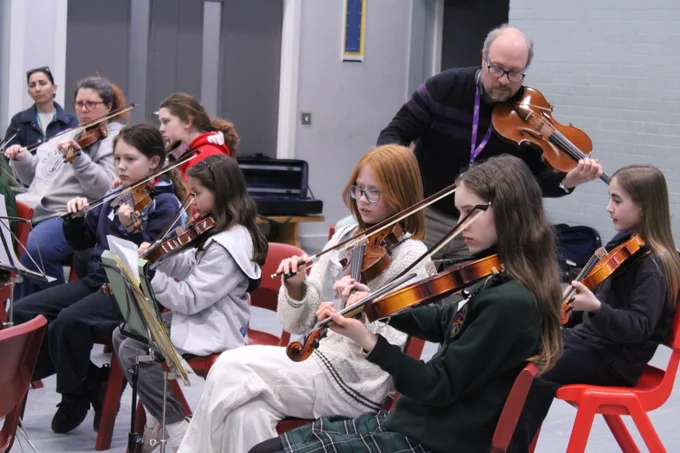 Group of young students seated in a classroom playing violins during a music lesson.