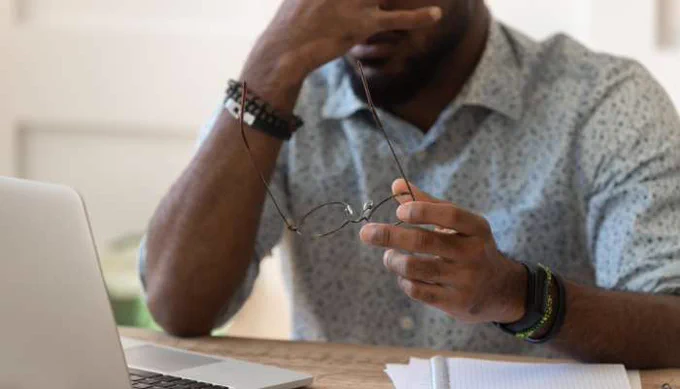  Man looking fatigued at desk holding glasses, representing why do you consistently feel off despite healthy habits and low energy issues
