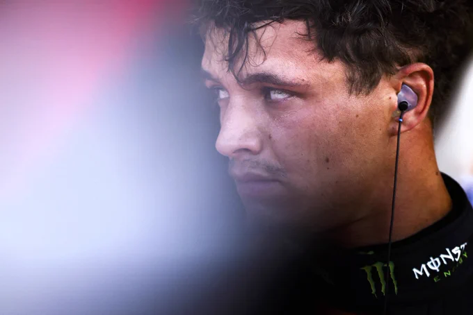 A close-up shot of Lando Norris looking to the side with headphones in his ear.