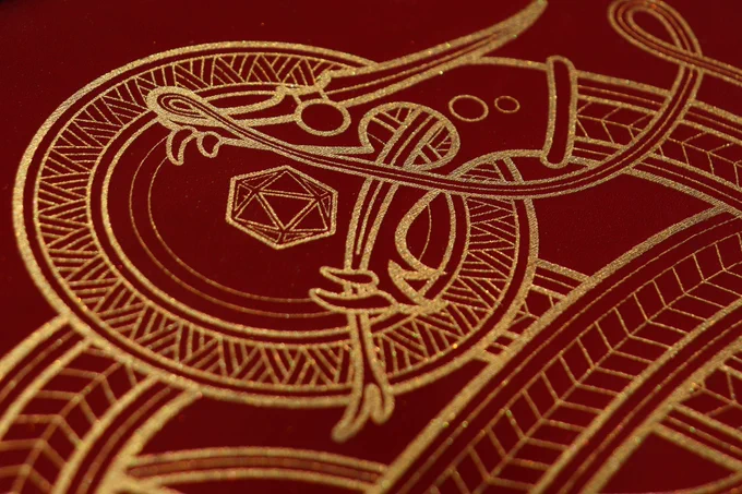A close up a red leather panel depicting a golden Norse style dragon, trying to devour a D20