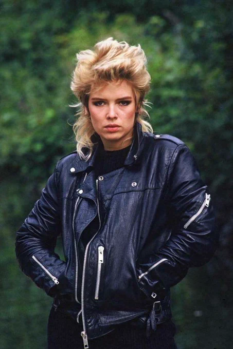 Promotional image of Kim Wilde circa 1981, taken during the “Kids In America” debut era, featuring her signature blonde hair and black leather jacket against a natural outdoor backdrop.