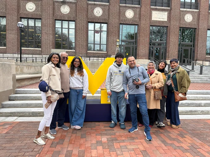A family standing in front of a giant block M in front of the U-M Hatcher Library.