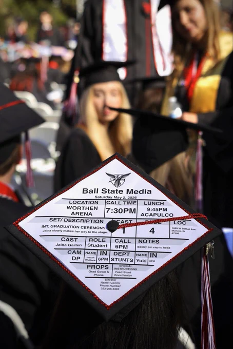 A Ball State University graduate's decorated cap is displayed at commencement, styled as a film production call sheet reading "Ball State Media" with details including the location (Worthen Arena), call time (7:30PM), and the set description "INT. Graduation Ceremony — Jaina slowly makes her way to the stage."