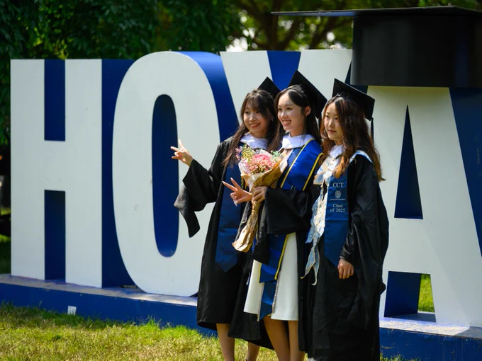 students in grad regalia pose in front of a sign saying "HOYA"