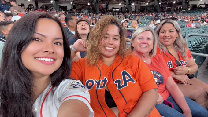 Group of four women wearing Houston Astros jerseys and shirts sitting together in stadium seats at a baseball game.