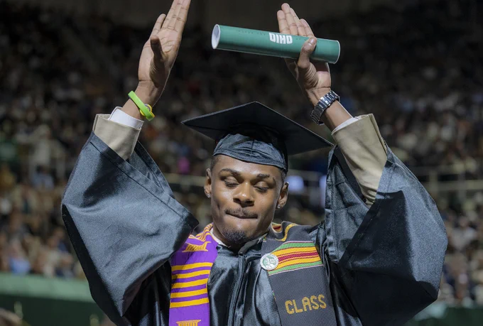 Graduate throwing hands into air as they come off the graduation stage