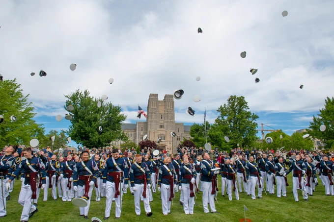 Cadets toss uniform covers into the air while standing in formation on the Drillfield, with Burruss Hall visible in the background.