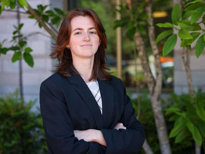 A picture of Julia Dieter wearing professional attire and standing in front of a building with greenery. 