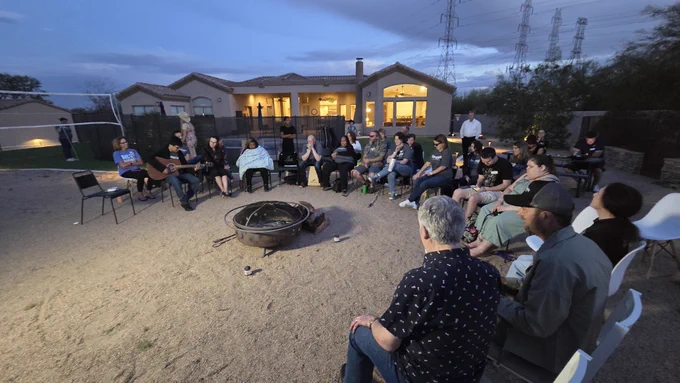 Attendees gathered around the fire pit at dusk with a guitar visible.