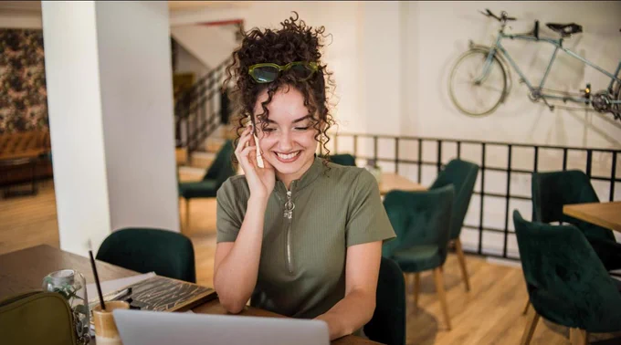 Woman with curly hair staring at computer screen smilling