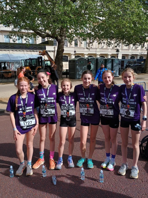 Six young girls in purple running t-shirts and medals smile after finishing a race.