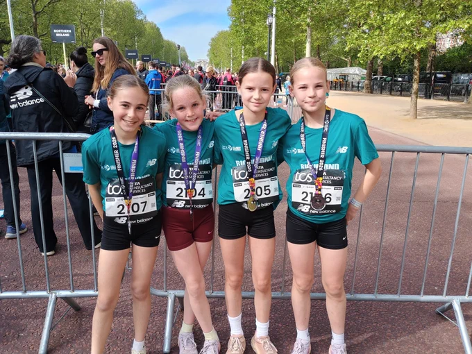 Four young girls in running gear and medals pose for a photo after a race.