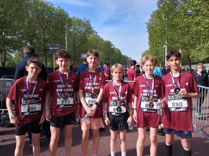 Six young boys in matching race t-shirts and medals pose for a photo after finishing a run.