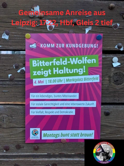 Das Bild zeigt ein Plakat, das an einer Holzwand mit Nieten & Klebeband befestigt ist. Es ist in auffälligen Pink- und Grünton gehalten & wirbt für eine Kundgebung mit dem Titel „Bitterfeld-Wolfen zeigt Haltung!“. Darunter steht Datum, Uhrzeit & Ort: „4.5., 18.00 Uhr | Marktplatz Bitterfeld“. 3 zentrale Botschaften sind in weißen Textboxen auf dem Plakat zu lesen: „Für ein lebendiges, buntes Miteinander.“, „Für soziale Gerechtigkeit & eine lebenswerte Zukunft.“ und „Für Vielfalt, Respekt und Demokratie.“ Unten auf dem Plakat steht der Slogan „Montags bunt statt braun!“ in einem grünen Kasten. Oben links ist ein Megafon-Symbol mit der Aufforderung „KOMM ZUR KUNDGEBUNG!“. Im unteren rechten Bereich des Plakats ist das Logo des „Netzwerk Zukunft. Miteinander gestalten!“ zu sehen. Über dem Plakat steht handschriftlich in roter Schrift: „Gemeinsame Anreise aus Leipzig: 17:22, Hbf, Gleis 2 tief“. Im unteren rechten Bildbereich ist das Logo von „Omas gegen Rechts Leipzig“ zu erkennen.
