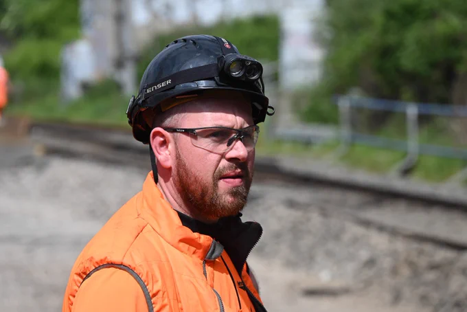 A photo of a track worker, wearing a black hard hat and PPE.